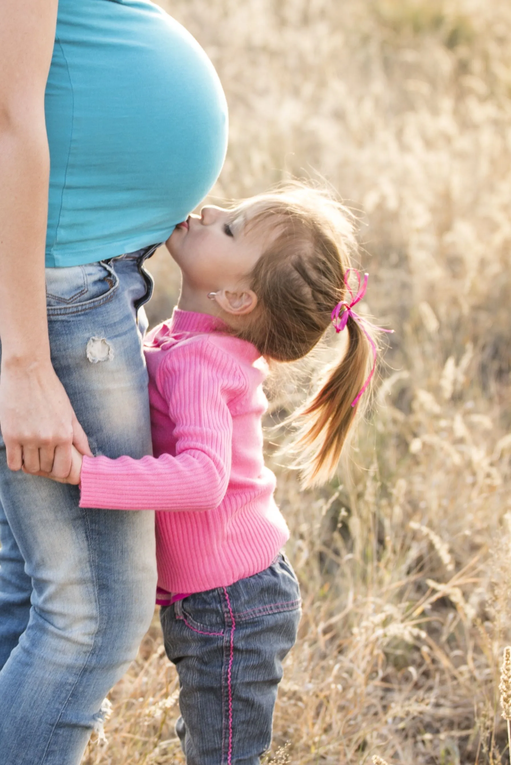 Young child kissing a pregnant surrogate mother's belly, representing families built through gestational surrogacy in Georgia